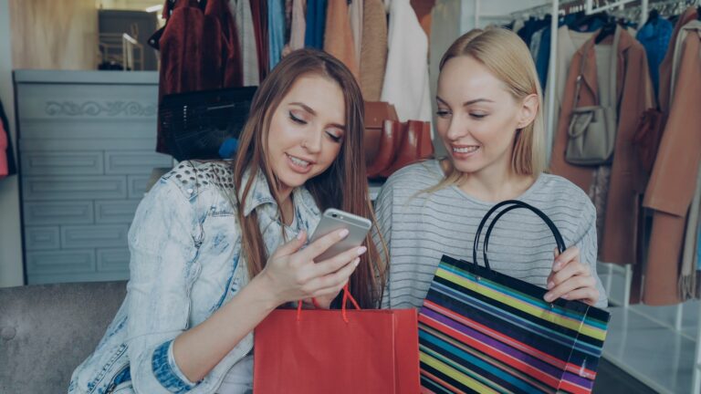 Two friends look at a phone after shopping.